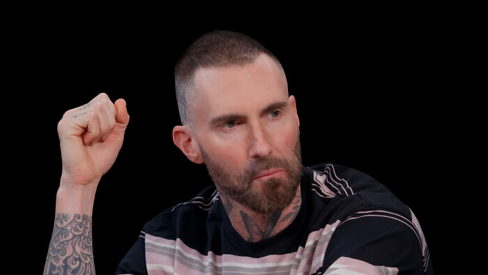 Singer Adam Levine looking thoughtful with his hand raised, recalling celebrity encounters