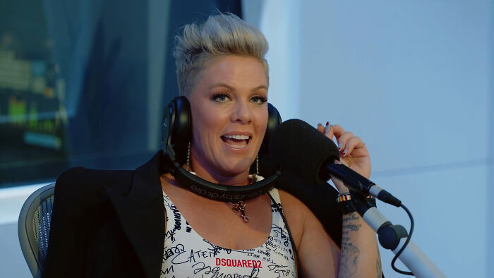 Pink speaking into a microphone with headphones around her neck during celebrity encounters interview.