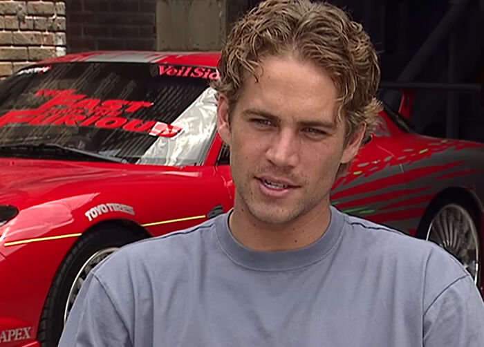 Paul Walker posing in front of a red sports car for celebrity encounters.