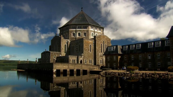 An imposing stone building with a dark roof reflected in calm water, evoking an eerie place. An imposing stone building with a dark roof reflected in calm water, evoking an eerie place.