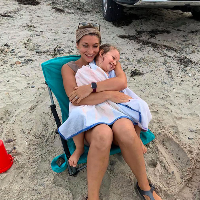 A woman, possibly Lindsay Clancy, with a child wrapped in a towel on a beach chair, hinting at her past life. A woman, possibly Lindsay Clancy, with a child wrapped in a towel on a beach chair, hinting at her past life.