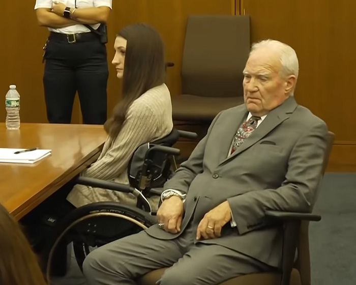 Lindsay Clancy in her wheelchair, seated next to an older man, with an odd sticker on her wheelchair. Lindsay Clancy in her wheelchair, seated next to an older man, with an odd sticker on her wheelchair.