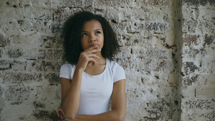 A thoughtful woman with curly hair against a brick wall, pondering stupid things people said.