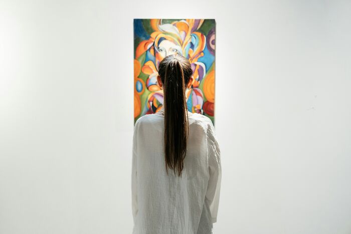 A woman with her back turned admiring a colorful painting on a white gallery wall at her creative work.
