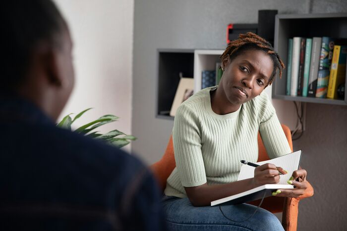 An African American woman takes notes in a notebook during an interview or therapy session at work.