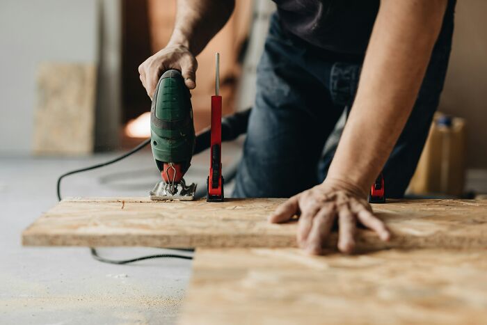 Hands using an electric jigsaw on a piece of wood, showing a carpentry task at work.