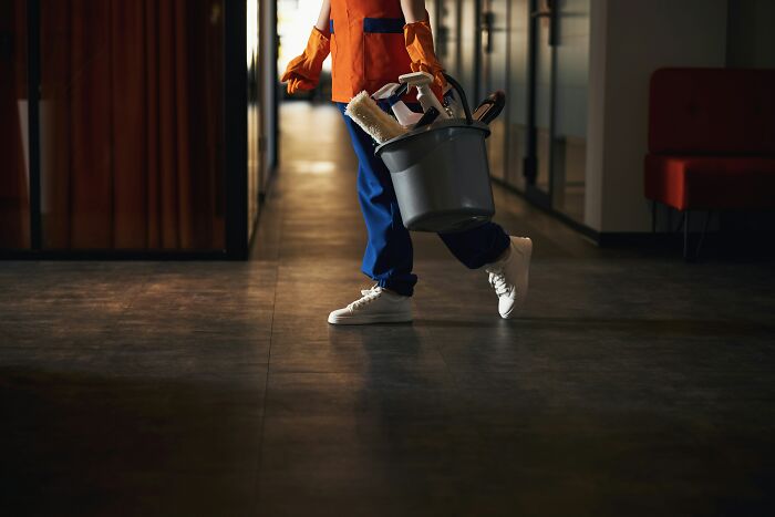 A janitor carrying a bucket of cleaning supplies down a hallway, representing blue-collar work in a changing economy.