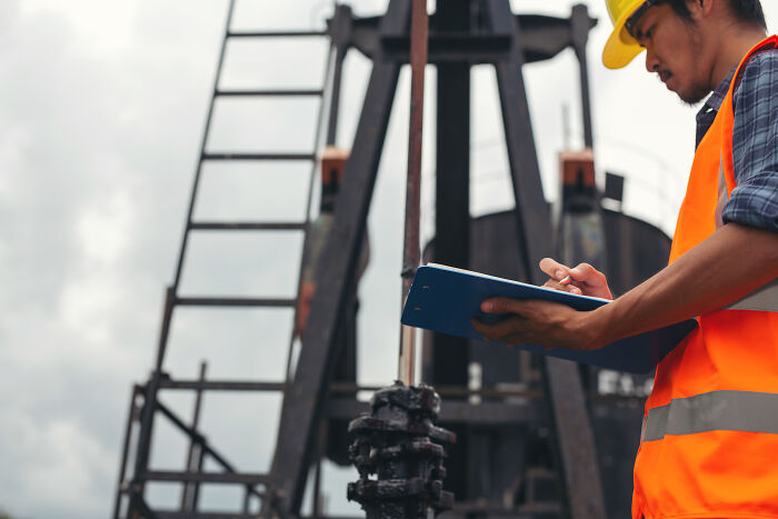 An engineer in safety gear taking notes on site, representing industrial work in the current economy.