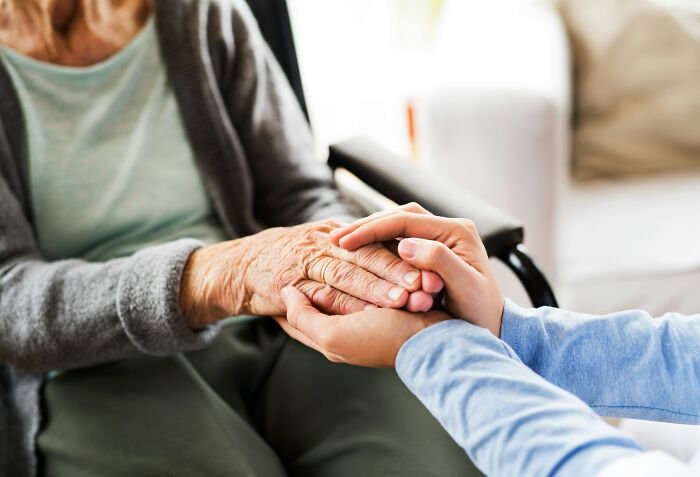 Close-up of a caregiver holding a senior person's hand, illustrating social support systems in a tough economy.