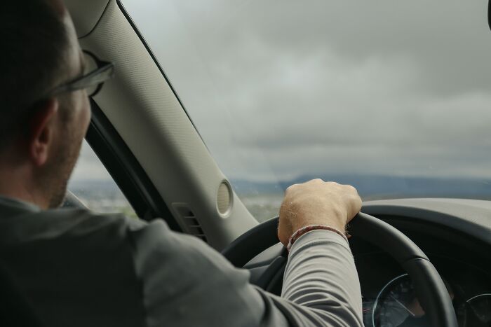 A man driving a car under a cloudy sky, representing daily life when the economy is in trouble.