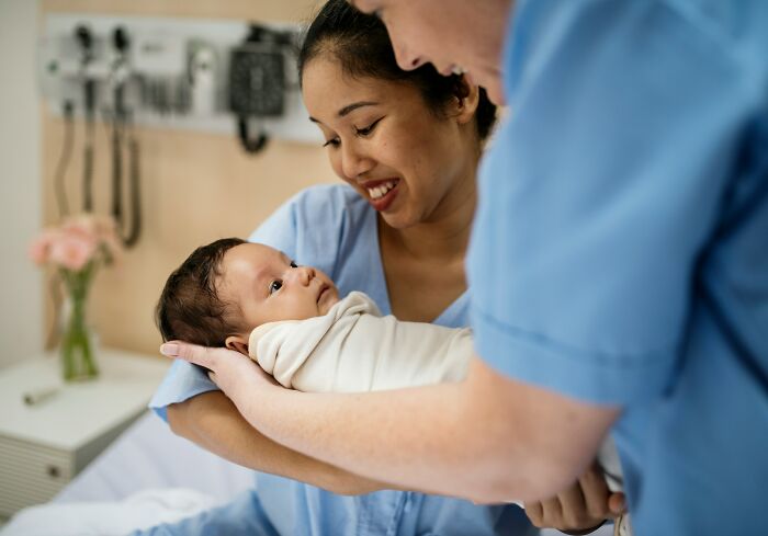 A nurse smiling at a newborn baby at work, representing healthcare services vital to the economy.