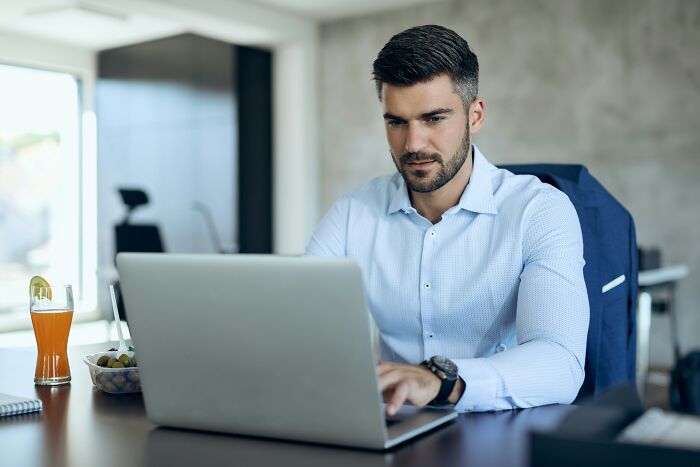 A focused man in a light blue shirt working on his laptop, representing shifting workplace dynamics