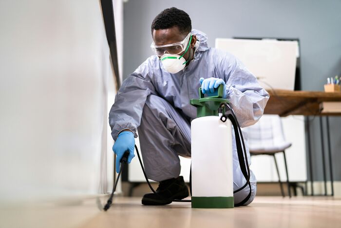 A man in a hazmat suit spraying a white wall, suggesting economic changes in service sectors