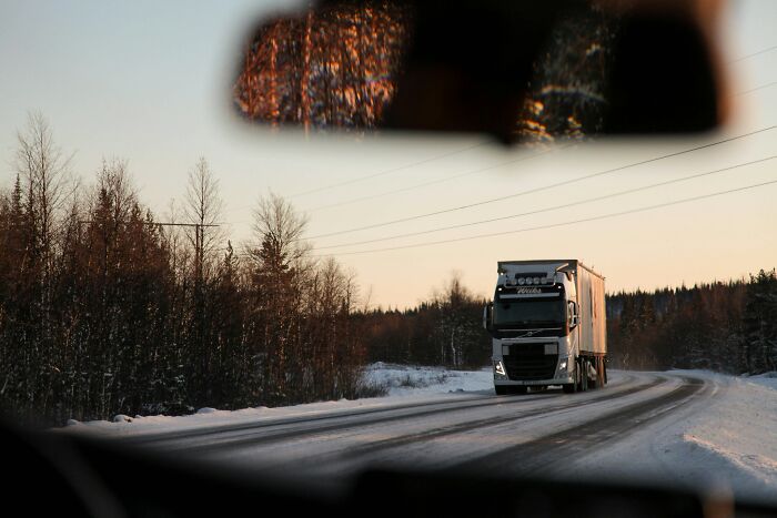 A white cargo truck driving on a snow-covered road under a sunset sky, symbolizing logistics and work.