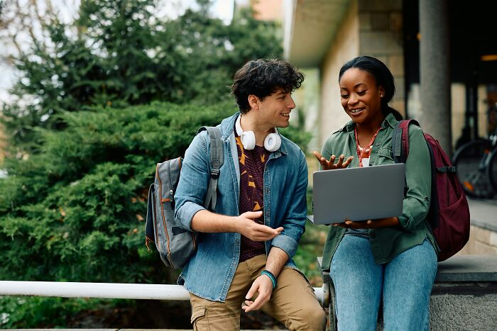 Two college students discussing on campus with a laptop, reflecting education and career plans in this economy.