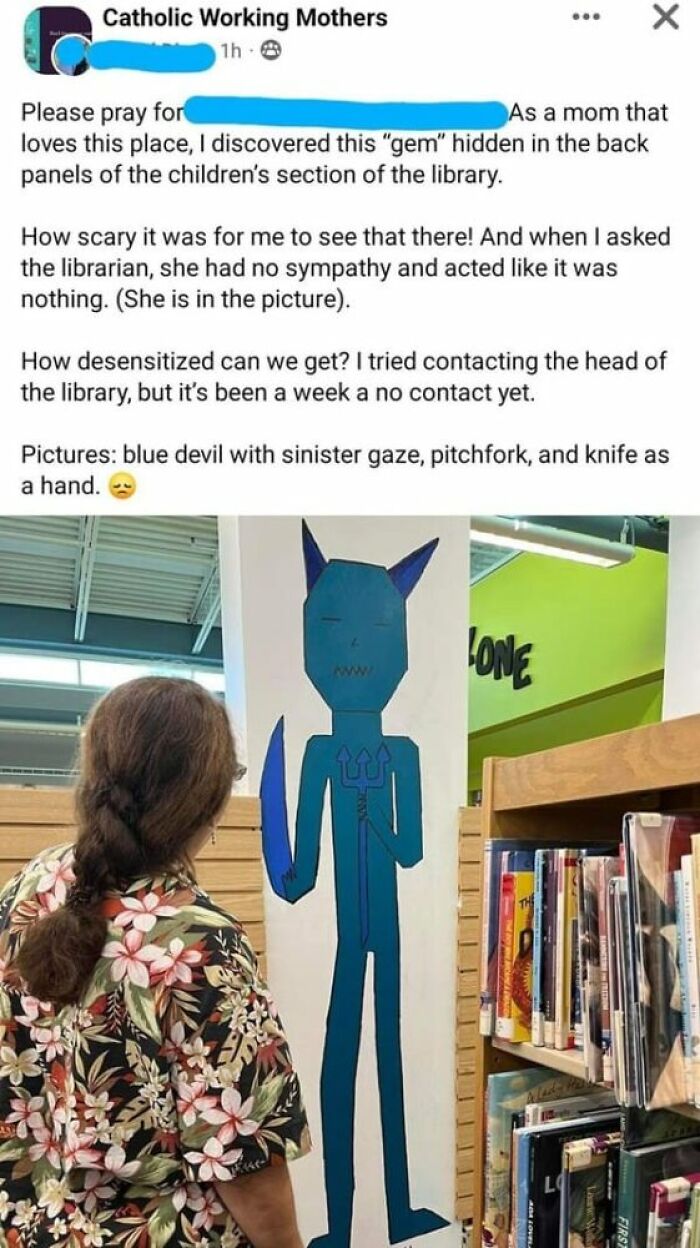 A woman stands near a tall, blue devil cutout with a pitchfork in a library, sharing unhinged thoughts on social media.