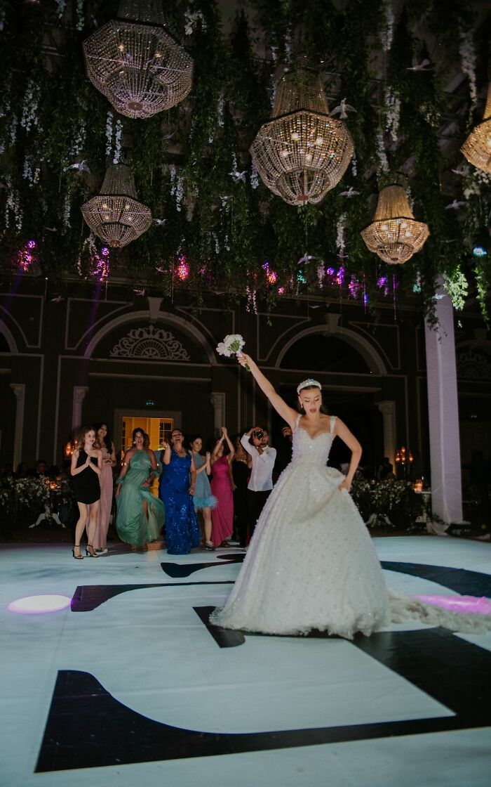 A bride in a white gown dancing and throwing her bouquet at a wedding, surrounded by guests, enjoying a wild turn.