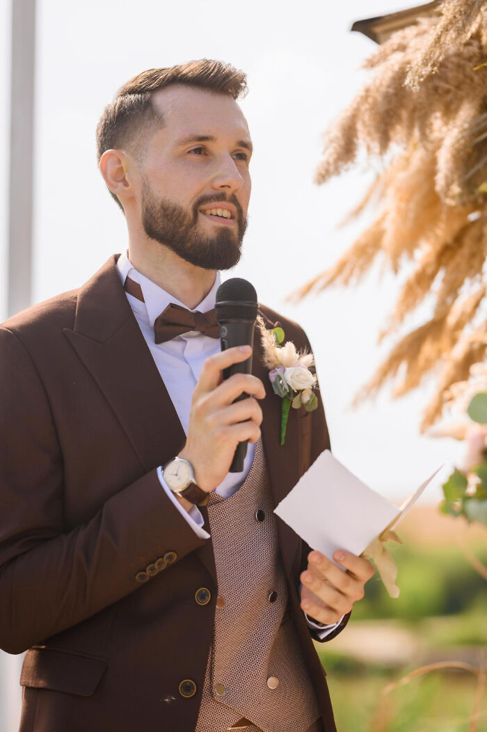 A man in a brown suit and bowtie giving a speech at a wedding, with pampas grass decor in the background, a wild turn of emotions.