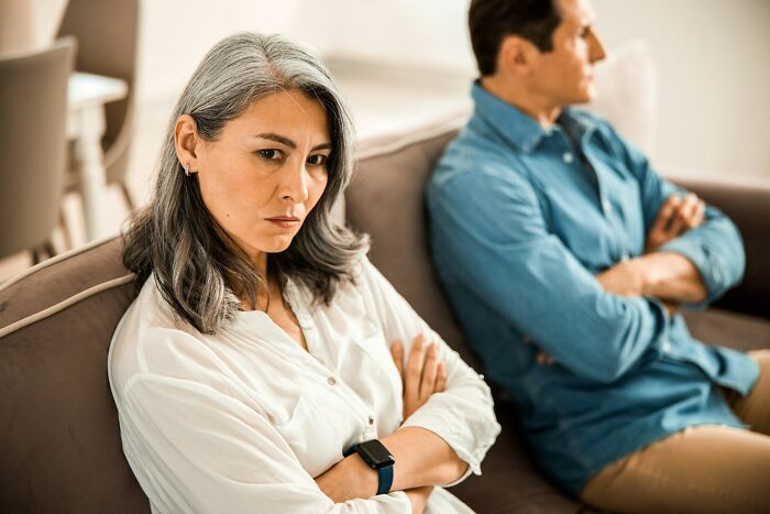 An upset woman with grey hair sits on a couch, arms crossed, during a wedding that took a wild turn.