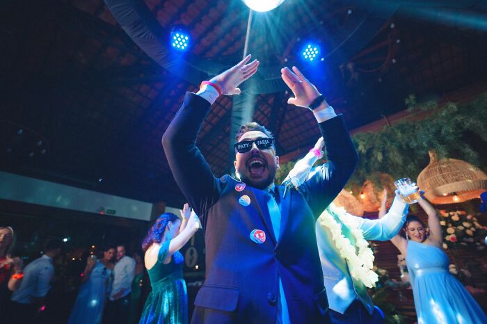 A man in sunglasses and a suit dancing enthusiastically under disco lights, a wild turn at a wedding party.