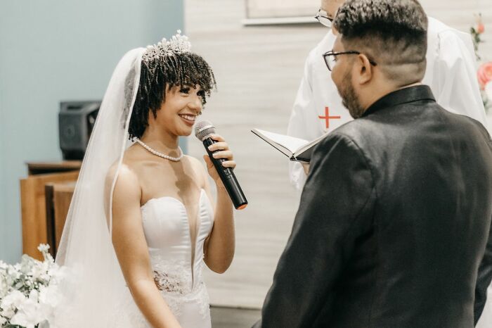 A joyous bride in a white gown and tiara speaks into a microphone during her wedding ceremony, a wild turn.