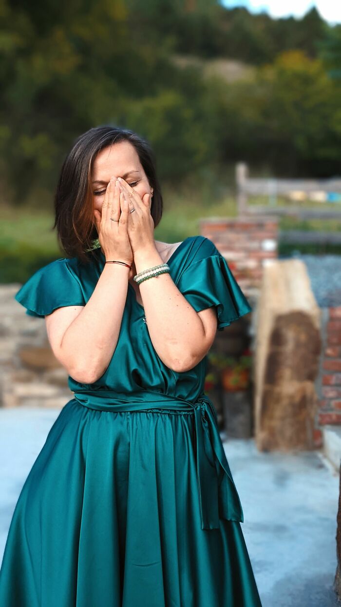 A woman in a green dress covering her face, laughing at a wild turn during a wedding.