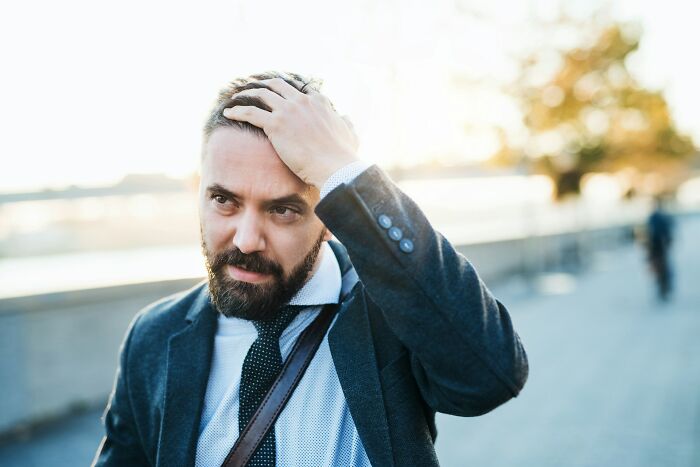 A man with a beard and a suit, looking stressed, possibly experiencing a wild turn in a situation.
