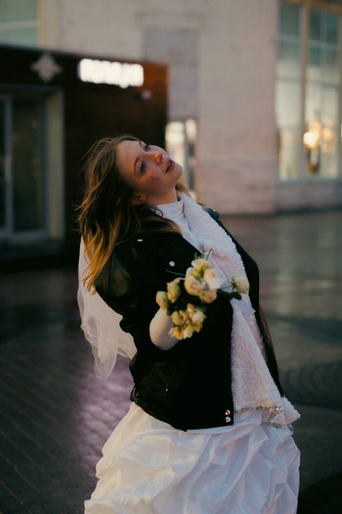 A woman in a wedding dress and leather jacket holds a bouquet, looking up, reflecting a wild wedding turn.