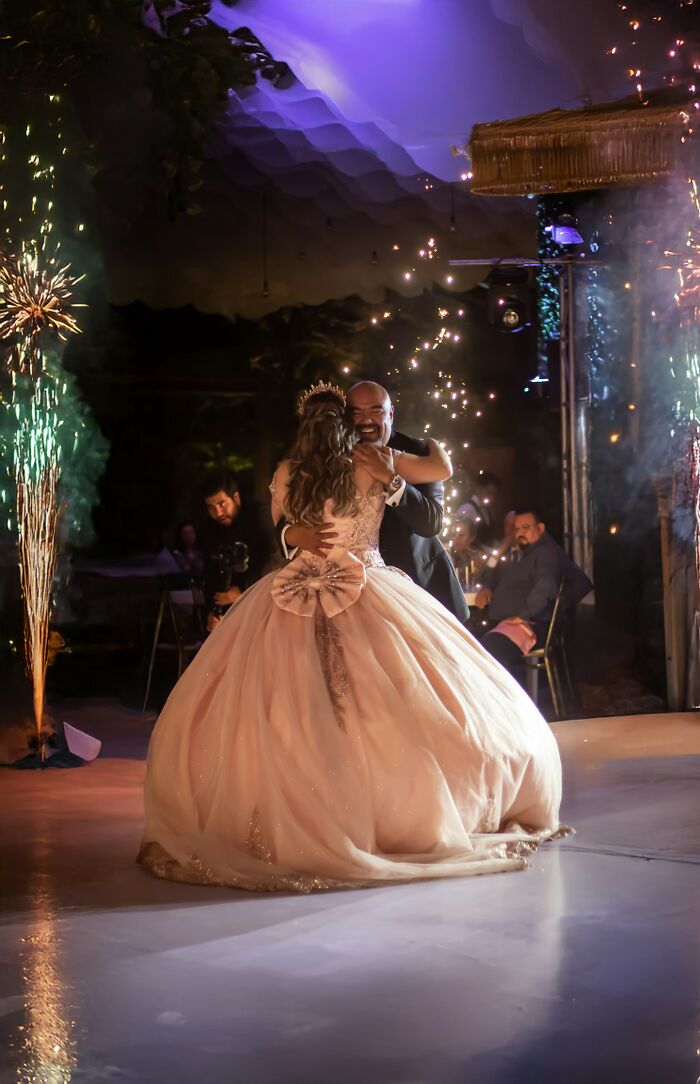 A young woman in a ballgown dancing with a man, with sparklers in the background at a wedding.