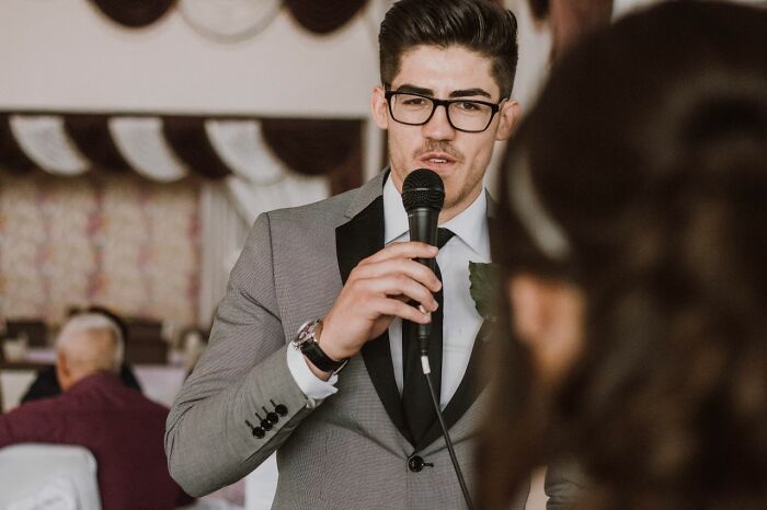 A man in glasses and a suit giving a speech at a wedding, a wild turn for the celebration.