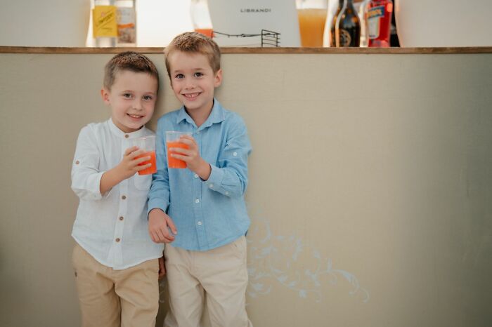 Two young boys holding orange drinks and smiling at a wedding, representing a wild turn of playful moments.