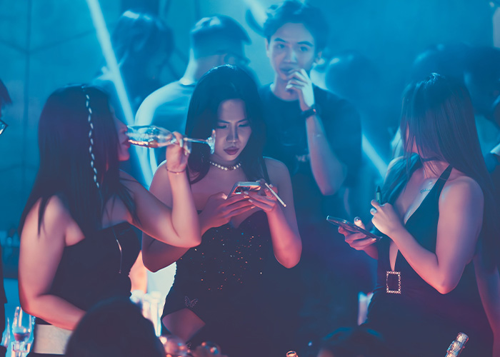 A group of women in a club, some looking at their phones, avoiding being bothered by men with a clever tactic.