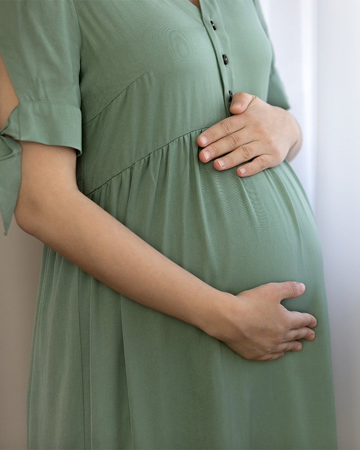 A pregnant woman in a green dress cradling her surrogate baby bump, reflecting on the disturbing truth.
