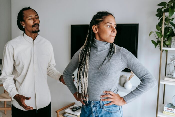 A man looking away from a woman with braids who looks annoyed, reflecting a girlfriend hurt by a guy who won't marry her.