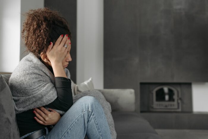 A woman sits on a couch, looking sad, representing a girlfriend hurt by a guy who won't say I love you or marry her.