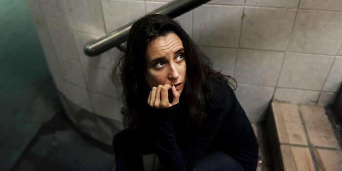 A woman looking up with a worried expression, biting her nails, appearing as if she overheard something she wasn't meant to hear.