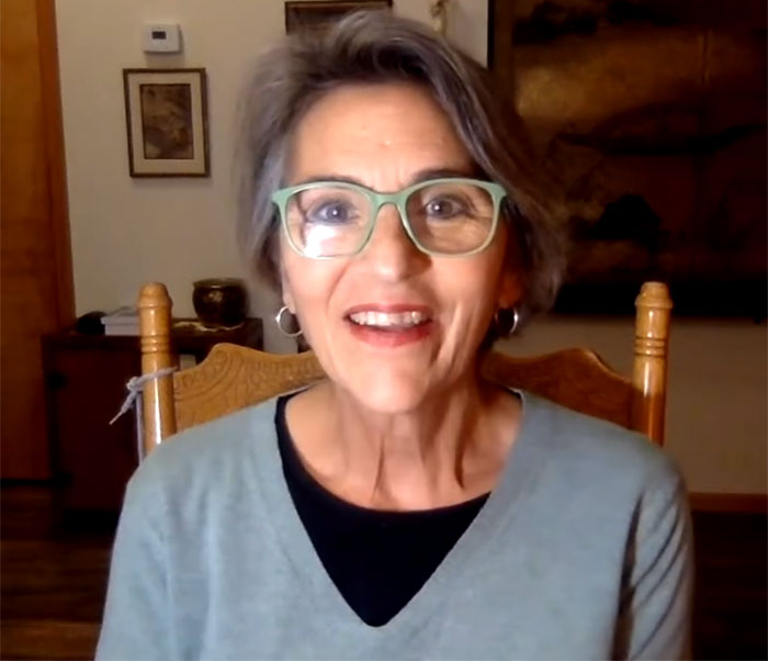 A woman with short grey hair and green glasses smiling at the camera, discussing her experience after she flatlined. A woman with short grey hair and green glasses smiling at the camera, discussing her experience after she flatlined.