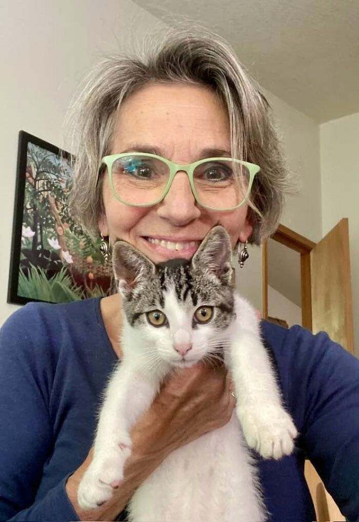 A woman with grey hair and green glasses holding a white and grey kitten, sharing her altered view on life after she flatlined. A woman with grey hair and green glasses holding a white and grey kitten, sharing her altered view on life after she flatlined.