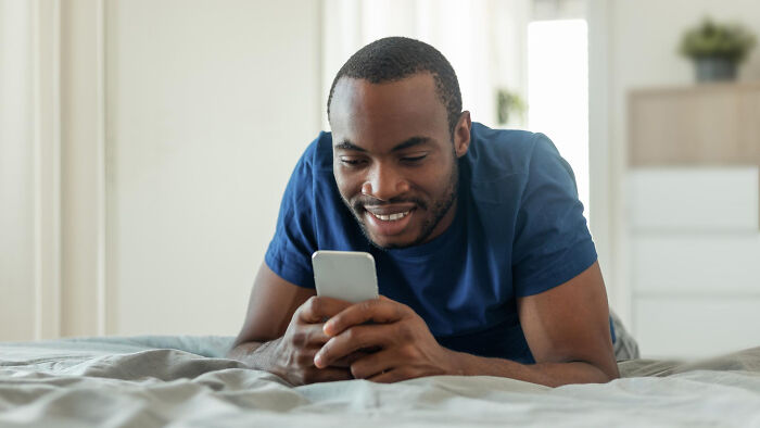 A smiling man looking at his phone, illustrating a woman's first date scenario. A smiling man looking at his phone, illustrating a woman's first date scenario.