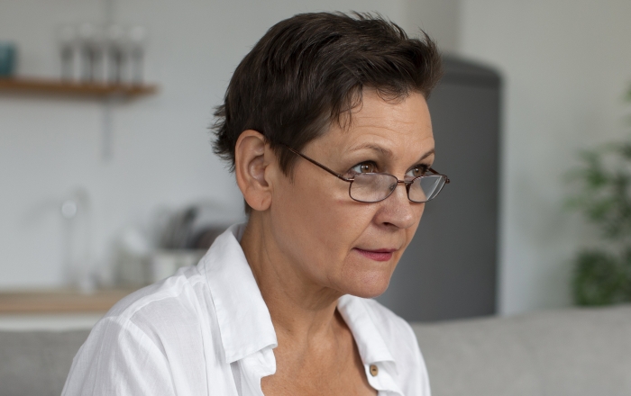 A woman wearing glasses with short hair looks off-camera, representing a MIL who thinks a shellfish allergy is fake. A woman wearing glasses with short hair looks off-camera, representing a MIL who thinks a shellfish allergy is fake.