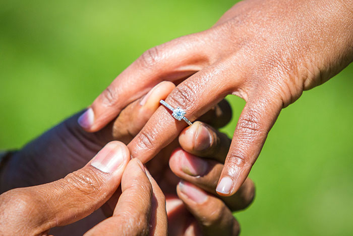 A close-up of a man placing an engagement ring on a woman's finger, symbolizing a marriage proposal.