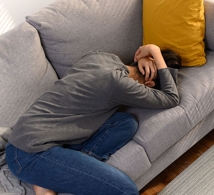 Woman curled on a sofa, looking sad and making the right choice by turning down marriage proposals.