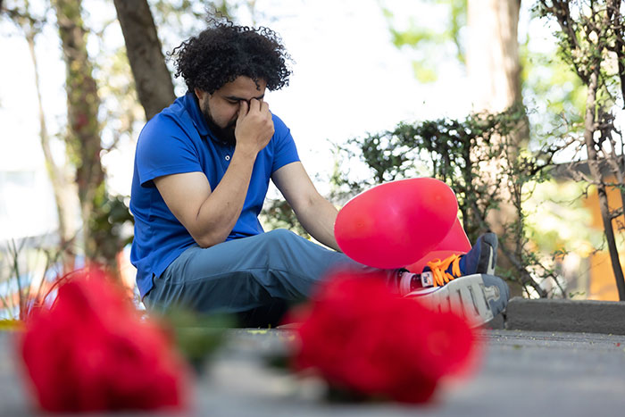 A man sits on the ground with a deflated balloon and flowers, reflecting on a marriage proposal being turned down.