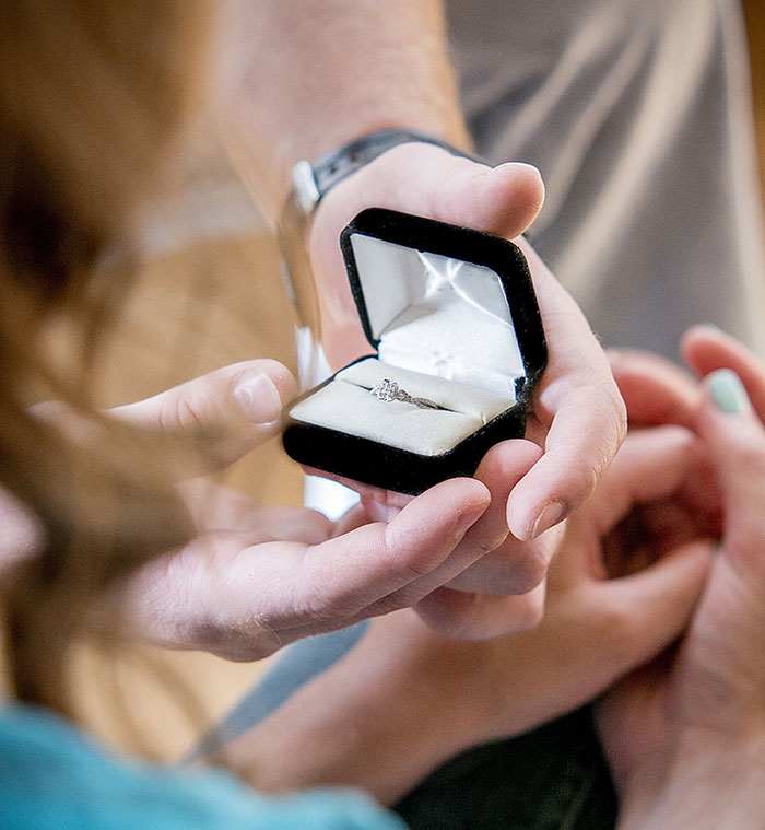 A man holding an open ring box with a diamond ring, proposing marriage.