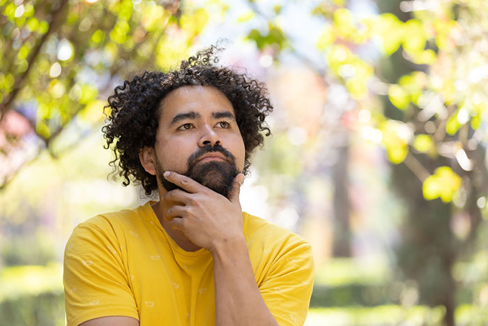 A thoughtful man with curly hair and beard, contemplating a marriage proposal.