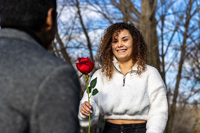 A woman smiling as a man offers her a red rose, representing a marriage proposal turned down.