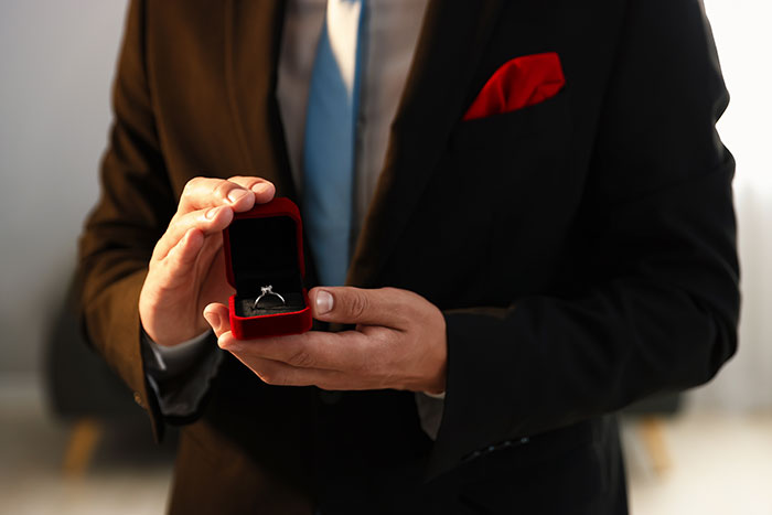 A man in a suit holding an open ring box, preparing to make a marriage proposal.