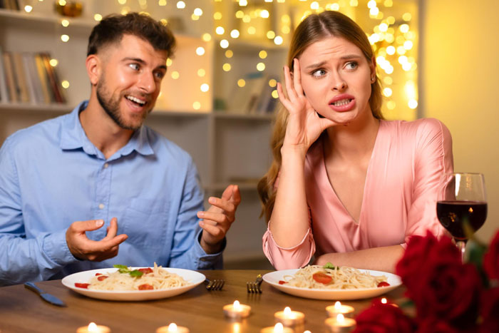 A woman looks annoyed while a man talks at dinner, showing women's nerves about men's nonsensical sentences.