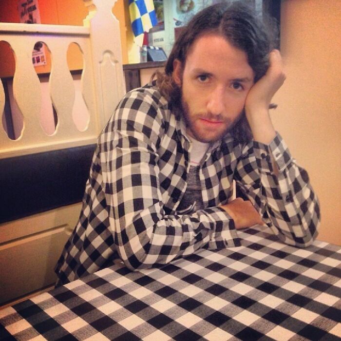 A man with a beard in a plaid shirt sits at a table with a matching plaid tablecloth, amazing synced.