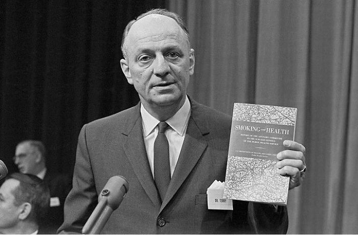 A vintage photo showing an event in medical history where a man holds up a Smoking and Health report